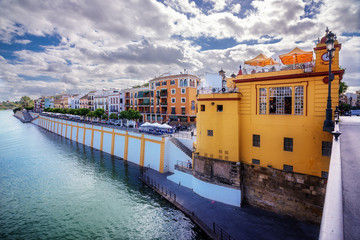 Obraz premium The old Triana lighthouse and the colorful houses of the riverbank of the Guadalquivir in Seville, Spain