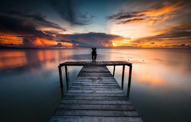 Fototapeta premium two girl stand together on the jetty during sunset with beautiful reflection