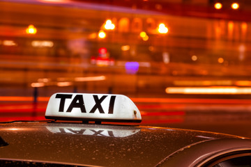 Shining Taxi inscription against passing cars on night street of big cit