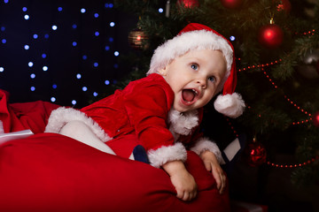 Fototapeta na wymiar Baby is sitting near Christmas tree with decoration