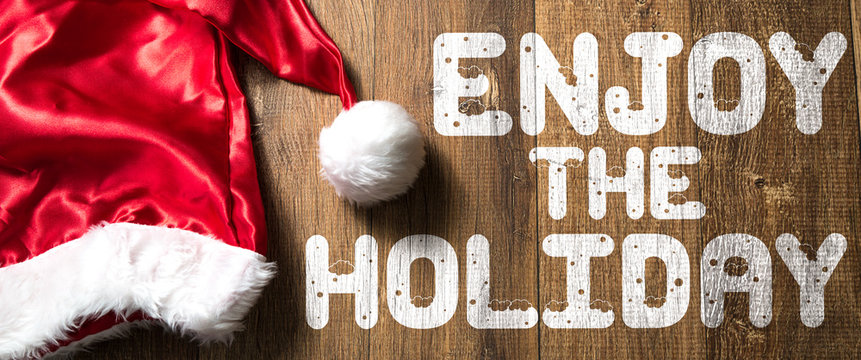 Enjoy the Holiday written on wooden background with Santa Hat
