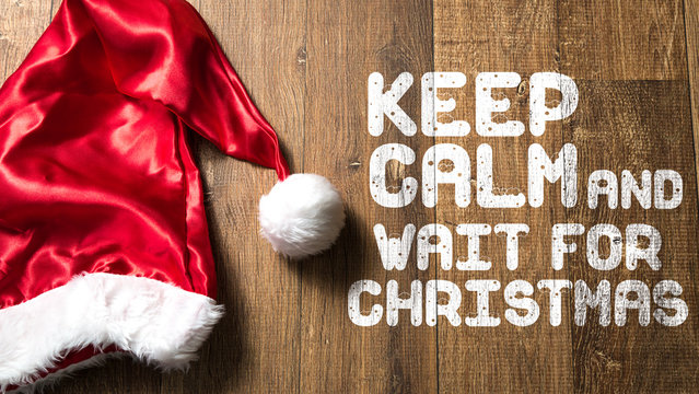 Keep Calm and Wait For Christmas written on wooden background with Santa Hat