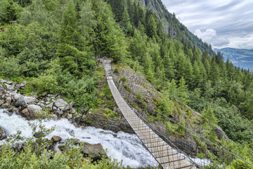 Fototapeta na wymiar Suspension bridge over fast mountain river