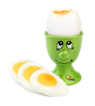 Cooked boiled egg in a green egg-cup with a painted face and slices of hard-boiled egg, isolated on white background.