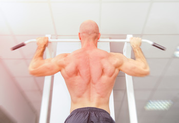 Fit bodybuilder fitness man doing pull ups at a gym with a bright light and filters applied suggesting movement and power at the workout