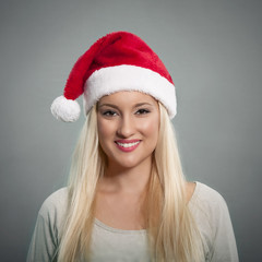 Beautiful young woman wearing Santa hat posing against gray background