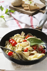Tagliatelle Pasta with cherry tomatoes in a pan  white wooden table and red checkered tablecloth