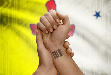 Barcode ID number on wrist of dark skin person and Canadian province flag on background - Nunavut