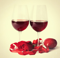 Composition with red wine in glasses, red rose, ribbon and decorative hearts on beige background