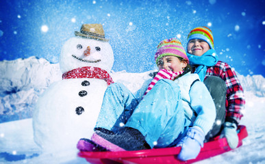 Little Girl and Boy Outdoors Sleding and Snowman Concept