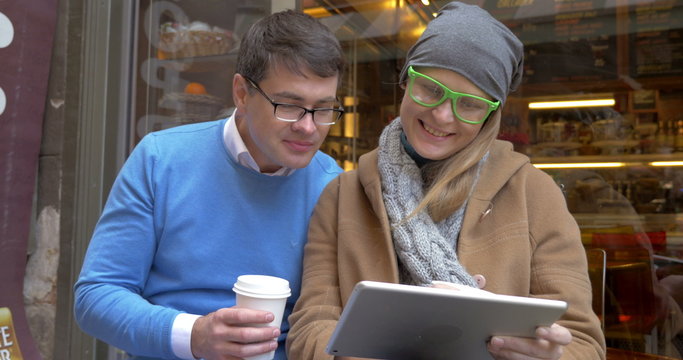 Young couple having coffee and using pad in city