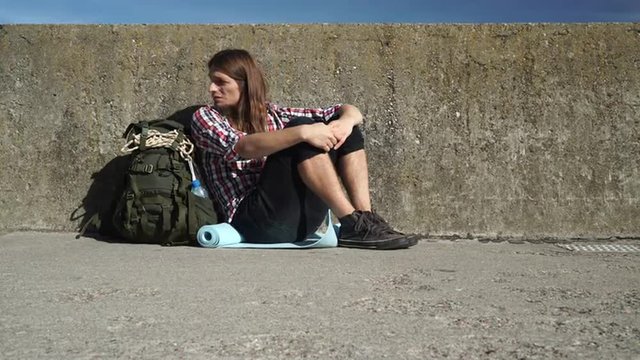 Man tourist backpacker sitting on grunge wall outdoor 4K