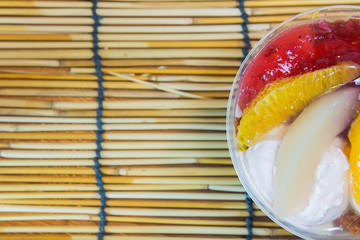 Ice cream and fruits in the plastic bowl on bamboo background.