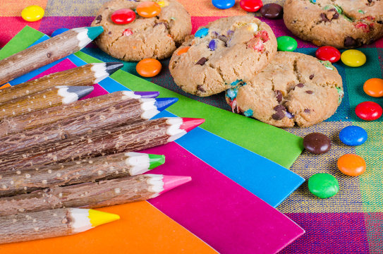 Fresh homemade muffins and cookies with color chocolate coated candies, colorful wooden pencils on a checkered kitchen towel. Free space for your text