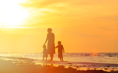 Fototapeta na wymiar mother and two kids walking on beach at sunset