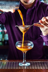 Barman pouring cocktail from shaker and serving it