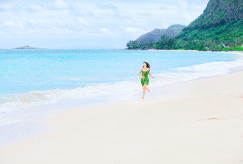 Beautiful teen girl in green dress running on Hawaiian beach