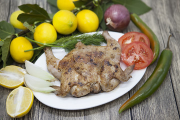 Fried chicken tapaka on porcelain plate with lemon and chilli onion  on the wooden background