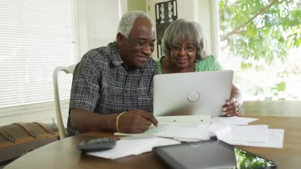 Happy senior African couple paying off bills on laptop - Powered by Adobe