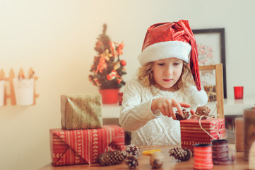 Obraz na płótnie Canvas child girl preparing gifts for christmas at home, cozy holiday interior