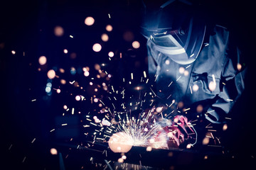 Employee welding steel with sparks using mig mag welder - focus on sparks. - obrazy, fototapety, plakaty