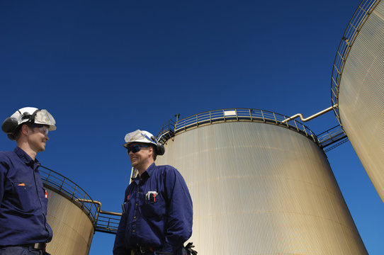 oil and gas workers with giant fuel-storage towers in background