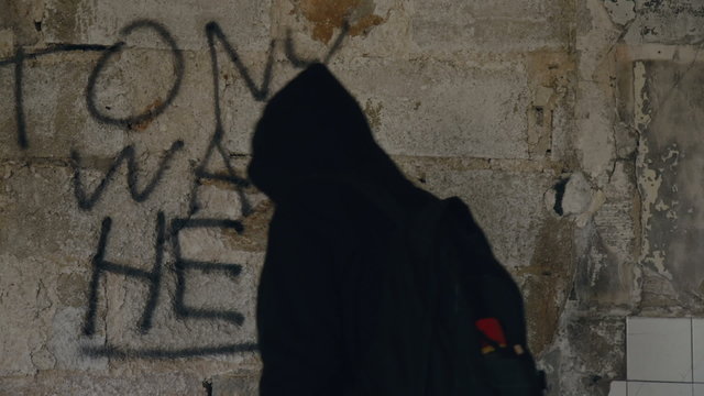 Hooded young man painting a graffiti message inside an abandoned ruined building