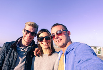 Three young friends taking selfie on sunny autumn day - Fashion  and hipsterstyle concept - Warm light filter look 