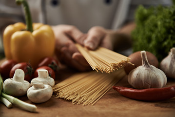 Woman chef cooking italian pasta with garlic,  pepper, mushrooms, tomatoes and greens on wooden...
