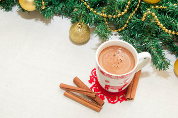 Obraz na płótnie Canvas Cup of hot cocoa or hot chocolate with cinnamon on tablecloth background with fir tree, traditional beverage for winter time