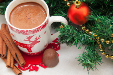 Cup of hot cocoa or hot chocolate with cinnamon on tablecloth background with fir tree, traditional beverage for winter time