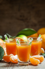 Fototapeta na wymiar Fresh juice of ripe mandarins in a small glass with striped stra