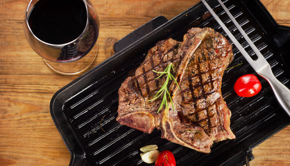 Grilled steak on grill pan with wine on wooden background.