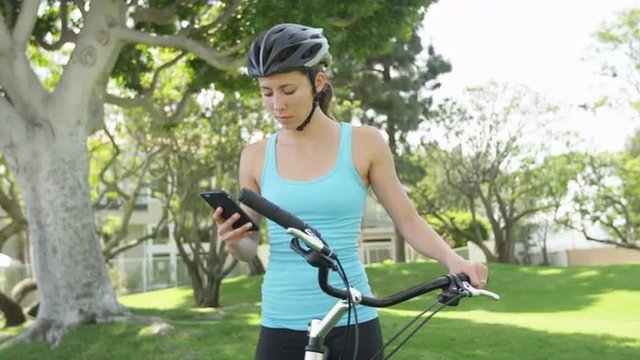 Young woman standing with bike using smartphone