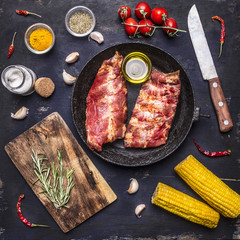 raw lamb ribs in a cast iron skillet, with a knife for meat, spices and herbs and corn on wooden rustic background top view