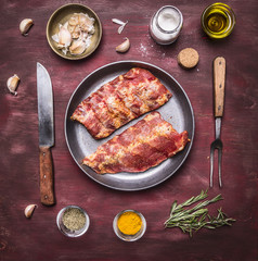 raw lamb ribs on a frying pan, with a knife and fork for the meat, spices and herbs on wooden rustic background top view