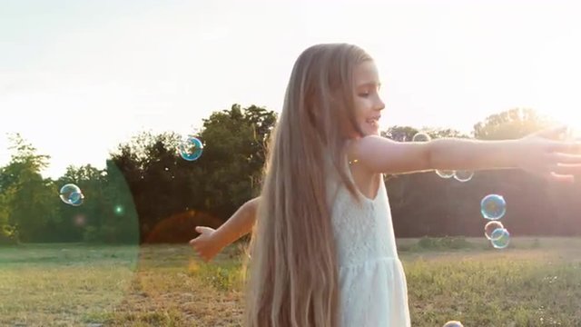 Girl spinning in the sunlight and soap bubbles. Lens flare. Child reaches for sunlight