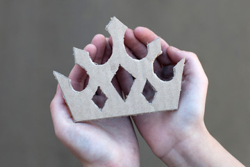 young homeless boy holds a cardboard crown