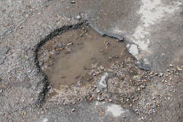 damage to tarmac road with potholes and puddles
