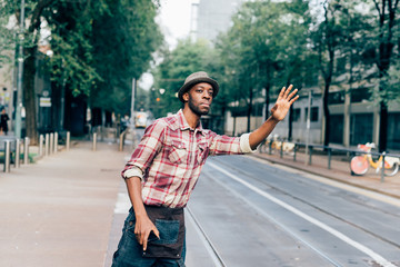 Portrait of young man waving hand for taxi on street