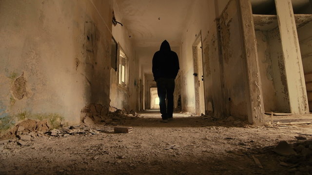 Hooded,troubled young man in wrecked abandoned building walking away