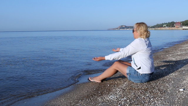 Woman sits on the beach of the Azov Sea and throwing stones into the water