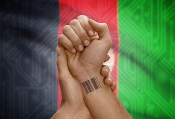 Barcode ID number on wrist of dark skinned person and national flag on background - Afghanistan