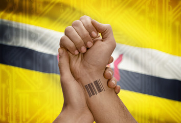 Barcode ID number on wrist of dark skinned person and national flag on background - Brunei