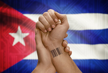 Barcode ID number on wrist of dark skinned person and national flag on background - Cuba