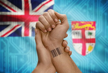 Barcode ID number on wrist of dark skinned person and national flag on background - Fiji