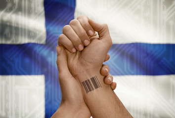 Barcode ID number on wrist of dark skinned person and national flag on background - Finland