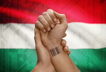 Barcode ID number on wrist of dark skinned person and national flag on background - Hungary