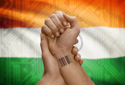 Barcode ID number on wrist of dark skinned person and national flag on background - India - Powered by Adobe