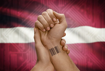 Barcode ID number on wrist of dark skinned person and national flag on background - Latvia